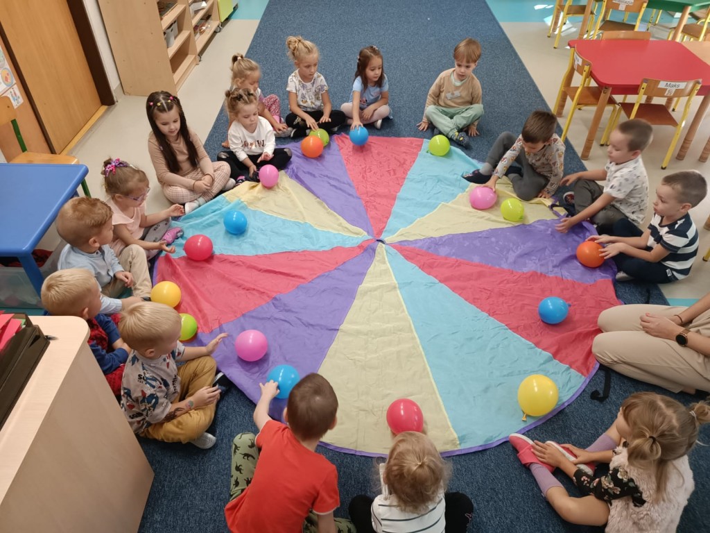 Dzieci siedzą w kręgu i trzymają w rękach kolorowe baloniki.
