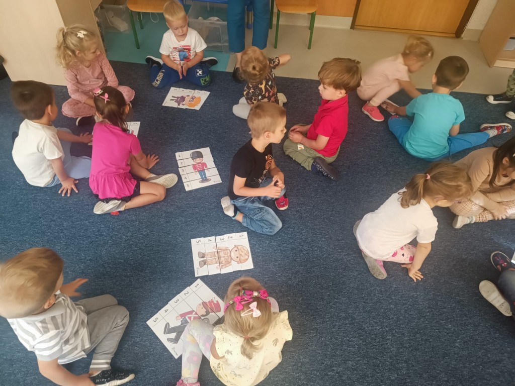 Chłopcy wraz z dziewczynkami siedzą na dywanie i układają puzzle
