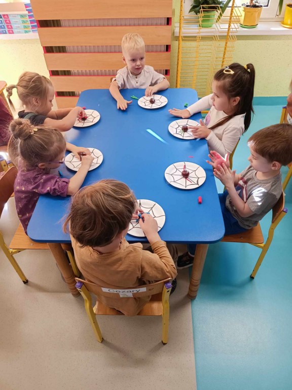 Dzieci siedzą przy stolikach i wykonują prace plastyczną