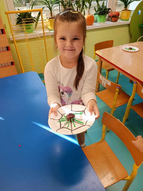 Dziewczynka prezentuje wykonanego pająka z kasztana na talerzyku papierowym