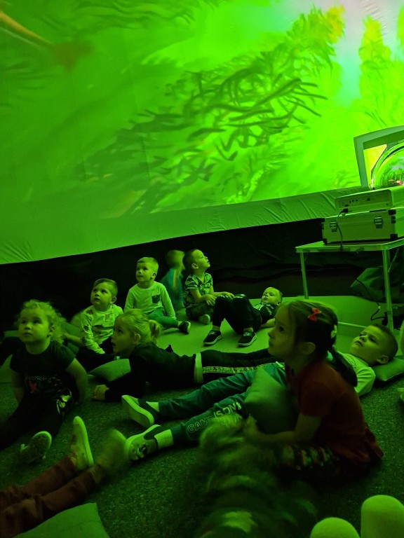 Dzieci siedzą w mobilnym kinie sferycznym i oglądają film o oceanarium.