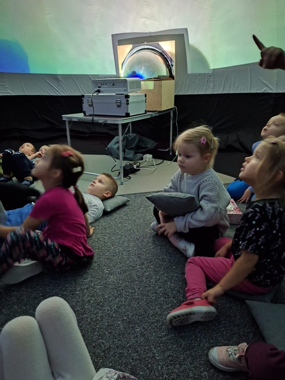 Dzieci siedzą w mobilnym ki9nie sferycznym i oglądają film.