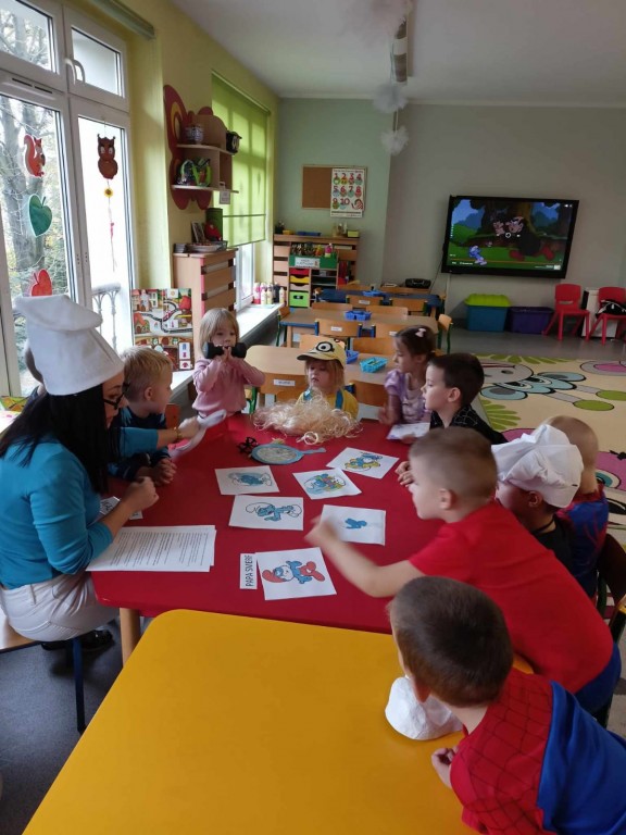 Dzieci wraz z nauczycielką siedzą przy stolikach i segregują obrazki ze smerfami