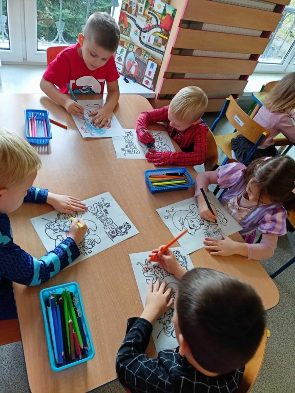 Dzieci kolorują przy stolikach obrazki ze smerfami