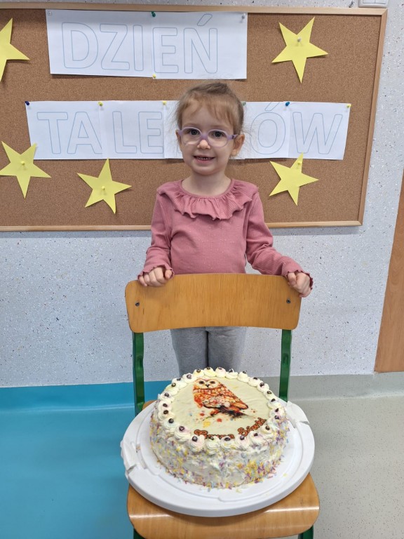 Dziewczynka stoi obok krzesełka, na którym jest postawiony tort