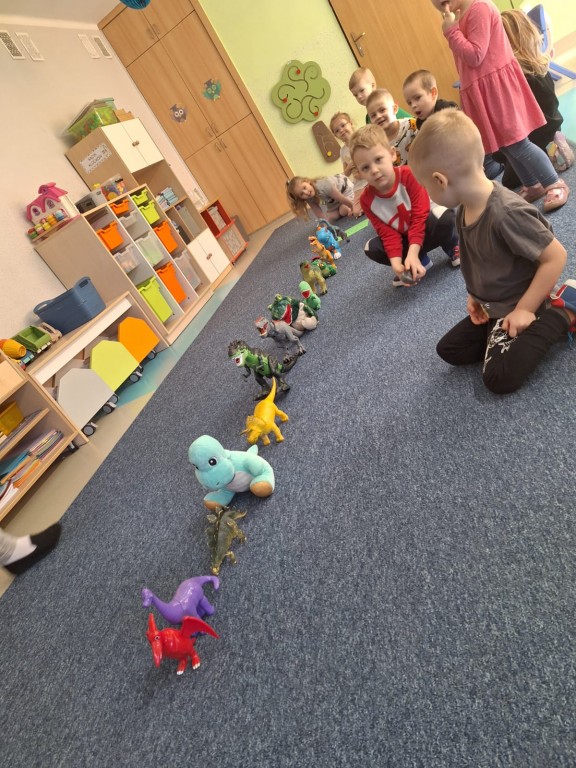 Dzieci ustawiają zabawki dinozaury w rzędzie