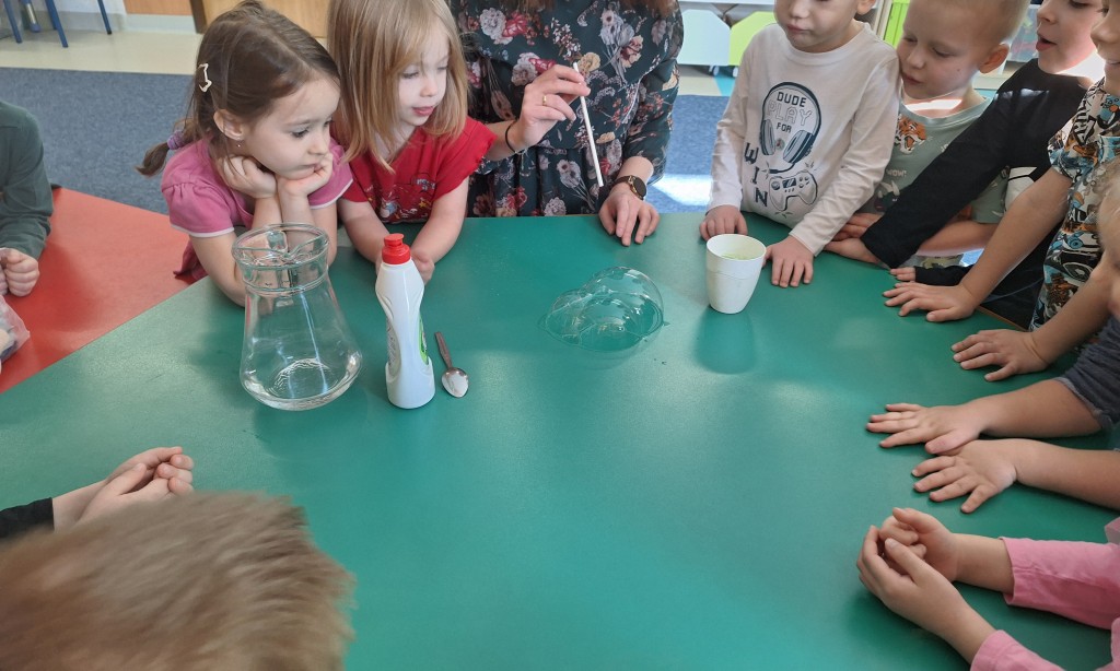 Nauczycielka pokazuje dzieciom jak zrobić bańki