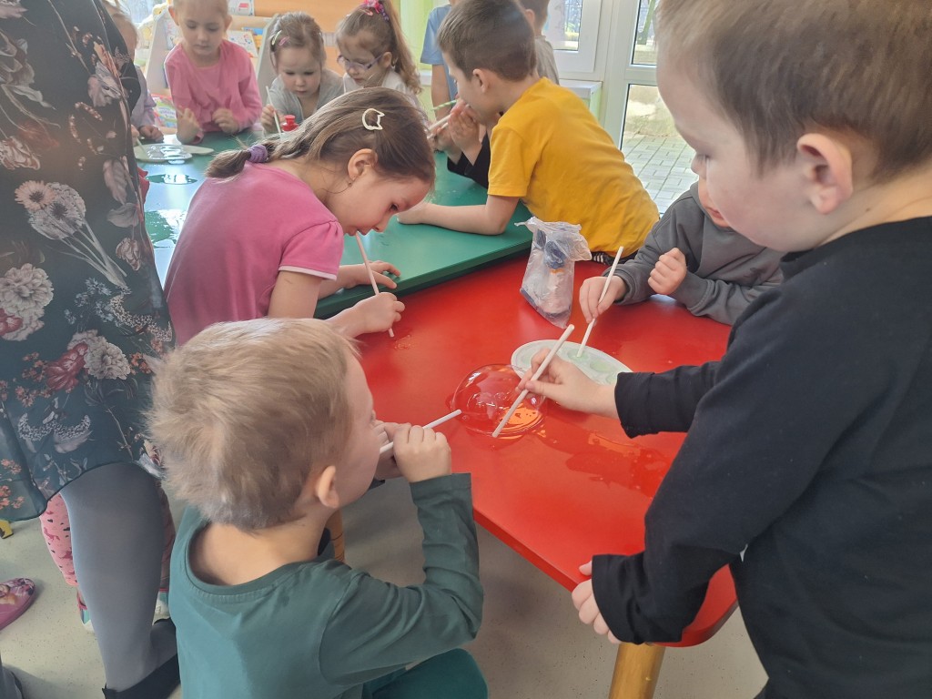 Dzieci za pomocą słomek dmuchają bańki przy stoliku