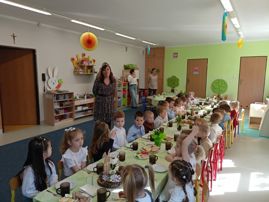 Dzieci siedza przy stolikach i jedza smiadanie wielkanocne