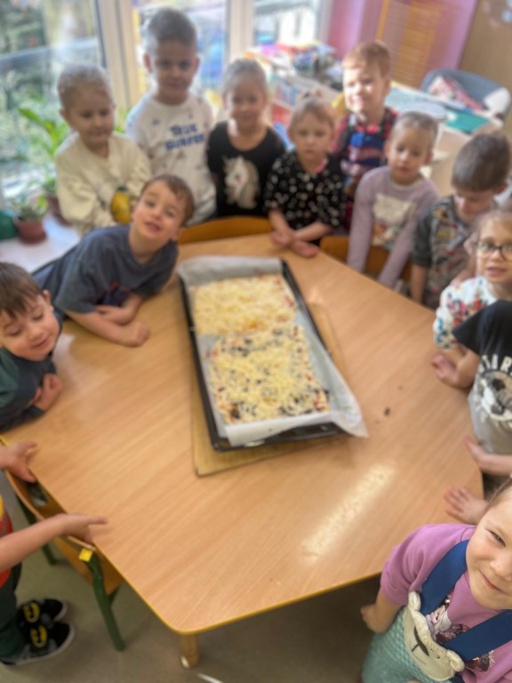 Dzieci stoją wokół stołu gdzie jest blacha z pizzą