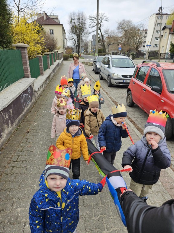 Dzieci z wychowawcą w koronach przed budynkiem przedszkol