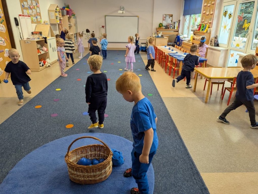 Dzieci szukają ukrytych w sali granatowych piłeczek