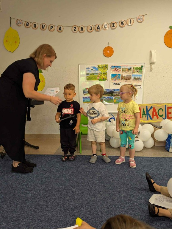 Troje dzieci przyjmują dyplomy i upominki