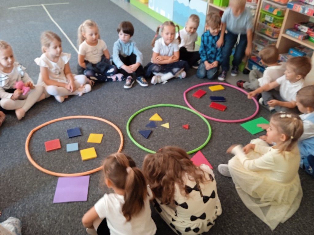 dzieci siedza w kole i przeliczaja figury geometryczne