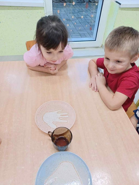 dzieci przy stolikach słuchają instruktażu