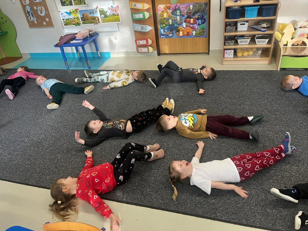 dzieci leżą na dywanie naśladując aniołki na śniegu