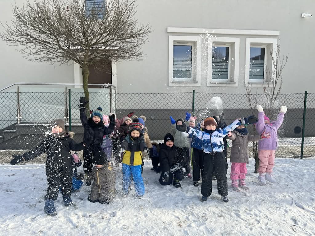 dzieci ustawione w grupie podrzucają w górę śnieg
