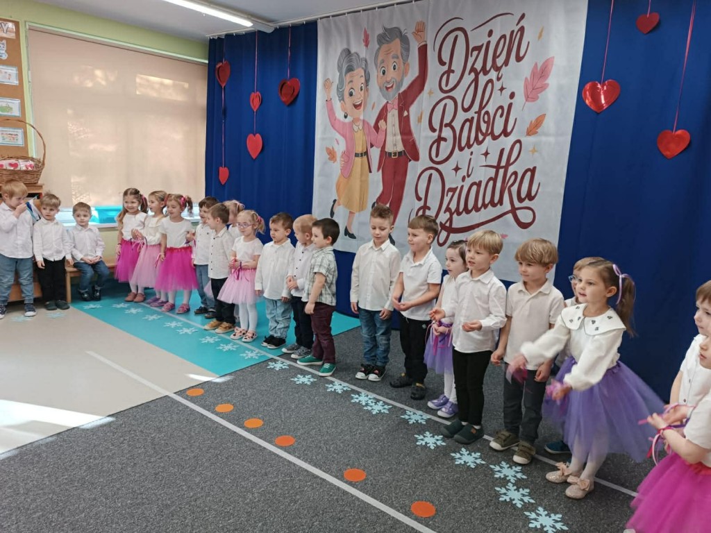 dzieci stoją  na tle dekoracji Dnia Babci i Dziadka