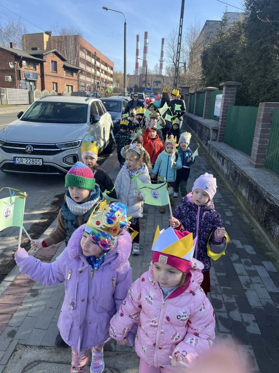 Dzieci w koronach idą uliczkami wokół przedszkola z proporczykami w ręku