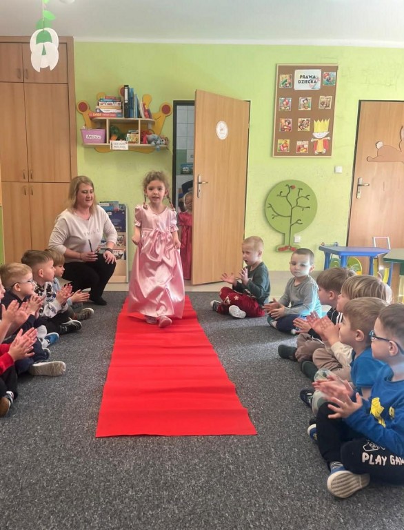 Dziewczynka  w balowej sukience przechodzi się po czerwonym dywanie