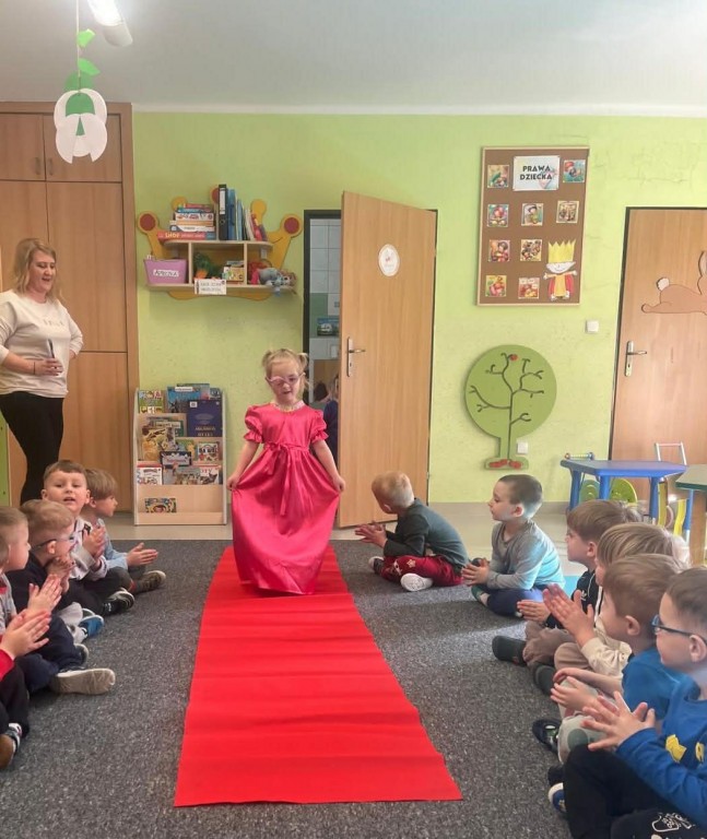 Dziewczynka  w balowej sukience przechodzi się po czerwonym dywanie