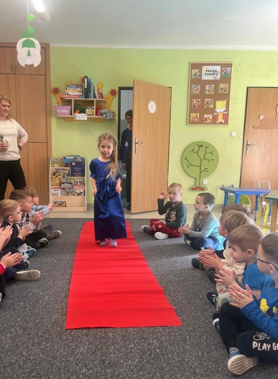 Dziewczynka  w balowej sukience przechodzi się po czerwonym dywanie