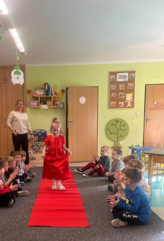 Dziewczynka  w balowej sukience przechodzi się po czerwonym dywanie