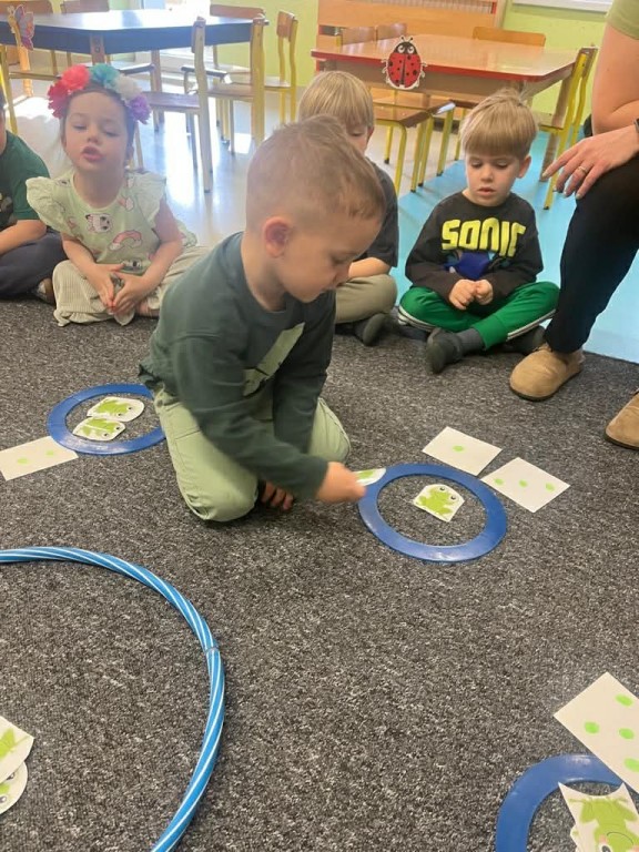 Chłopiec układa w stawie żabki zgodnie z liczbą oczek