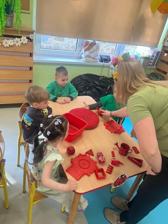 nauczyciel liczy zebrane przez dzieci przedmioty czerwone