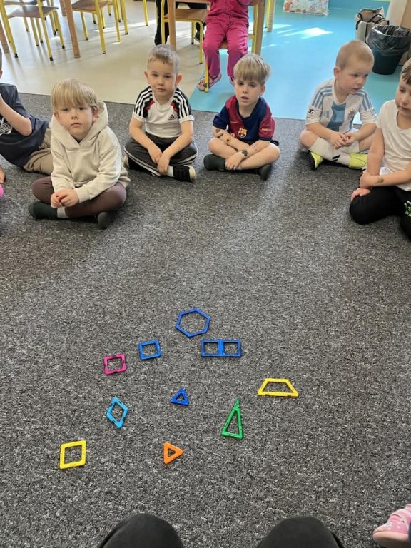 Dzieci przyglądają się wyłożonym na dywanie kształtom z klocków magnetycznych