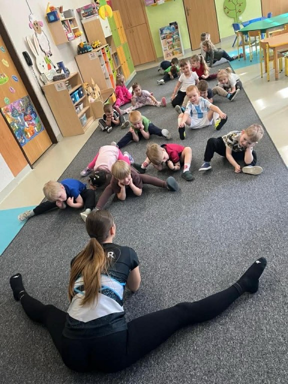 dzieci naśladując instruktorkę próbują zrobić półszpagat podparty