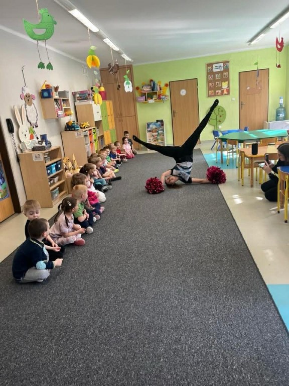 dzieci oglądają figury gimnastyczne wykonane przez instruktorkę