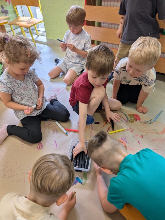 Dzieci rysują mazakami na dużym arkuszu papieru