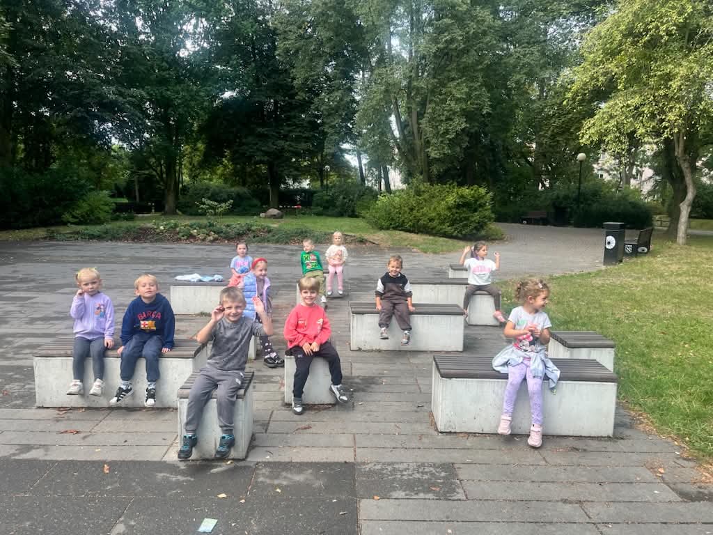 dzieci siedzą na kamiennych siedziskach w parku przed Domem Kultury